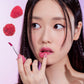 Woman applying lipstick with raspberries on a pink background, featuring the ETUDE brand.