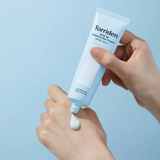 Hand holding a tube of Torriden cream against a light blue background
